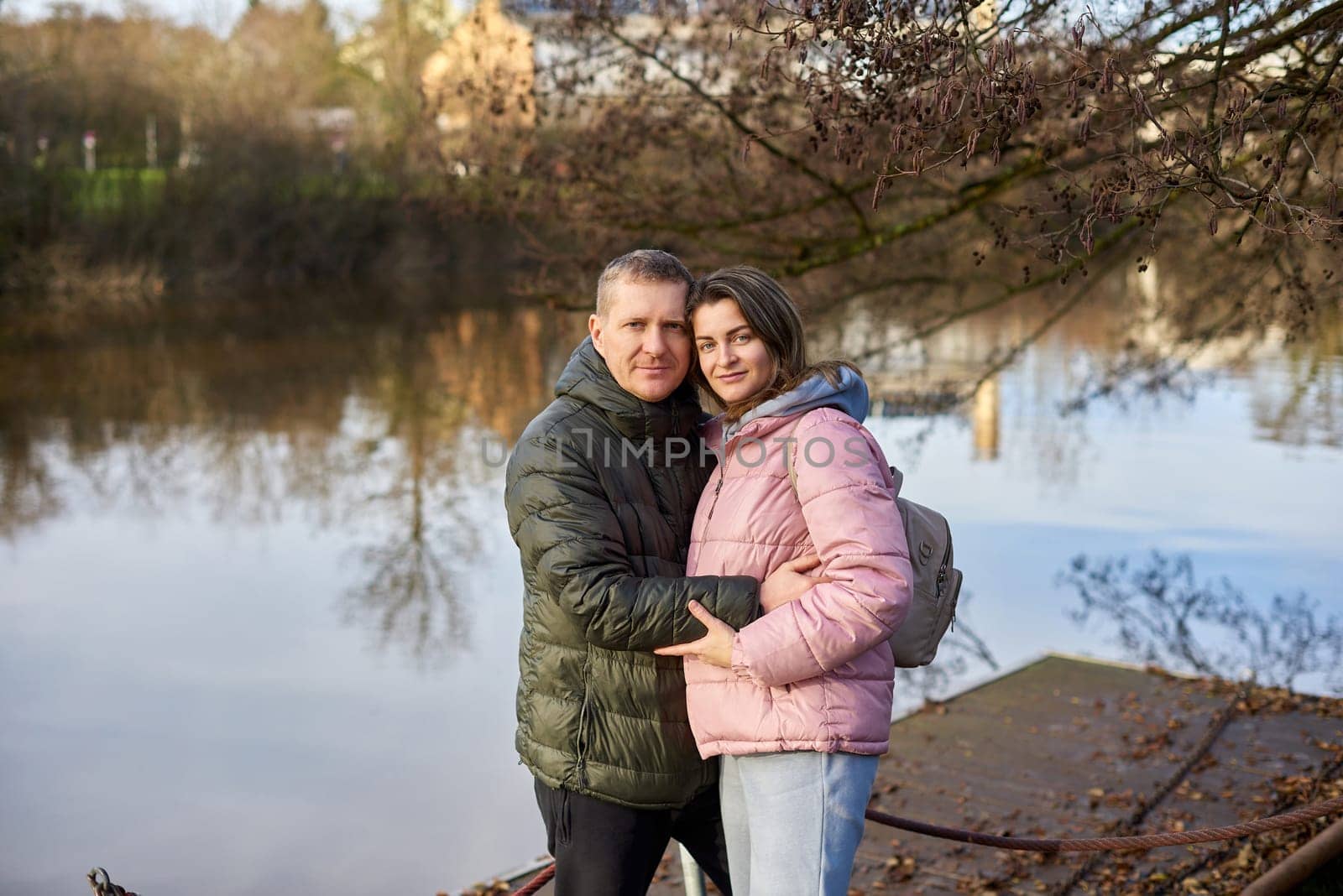 Loving couple on the shore of the pond in the park in autumn. A man and a woman. A couple, lovers on the shore of the lake on a walk. Autumn Romance by the Lake: Happy Couple's Lakeside Leisure. Seasons of Love: Couple's Tranquil Parkside Getaway by Andrii_Ko