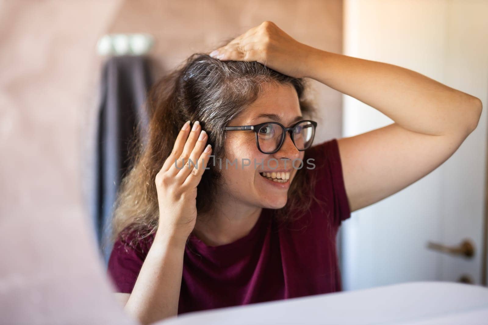 Gray haired surprised caucasian middle aged woman looking at grey hair head in mirror reflection