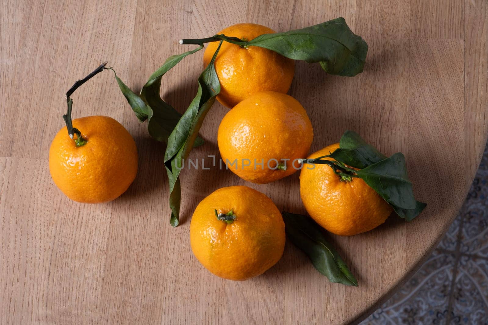 Several fresh ripe tangerines with leaves lie on a table with a round wooden bedstead. Selective focus.