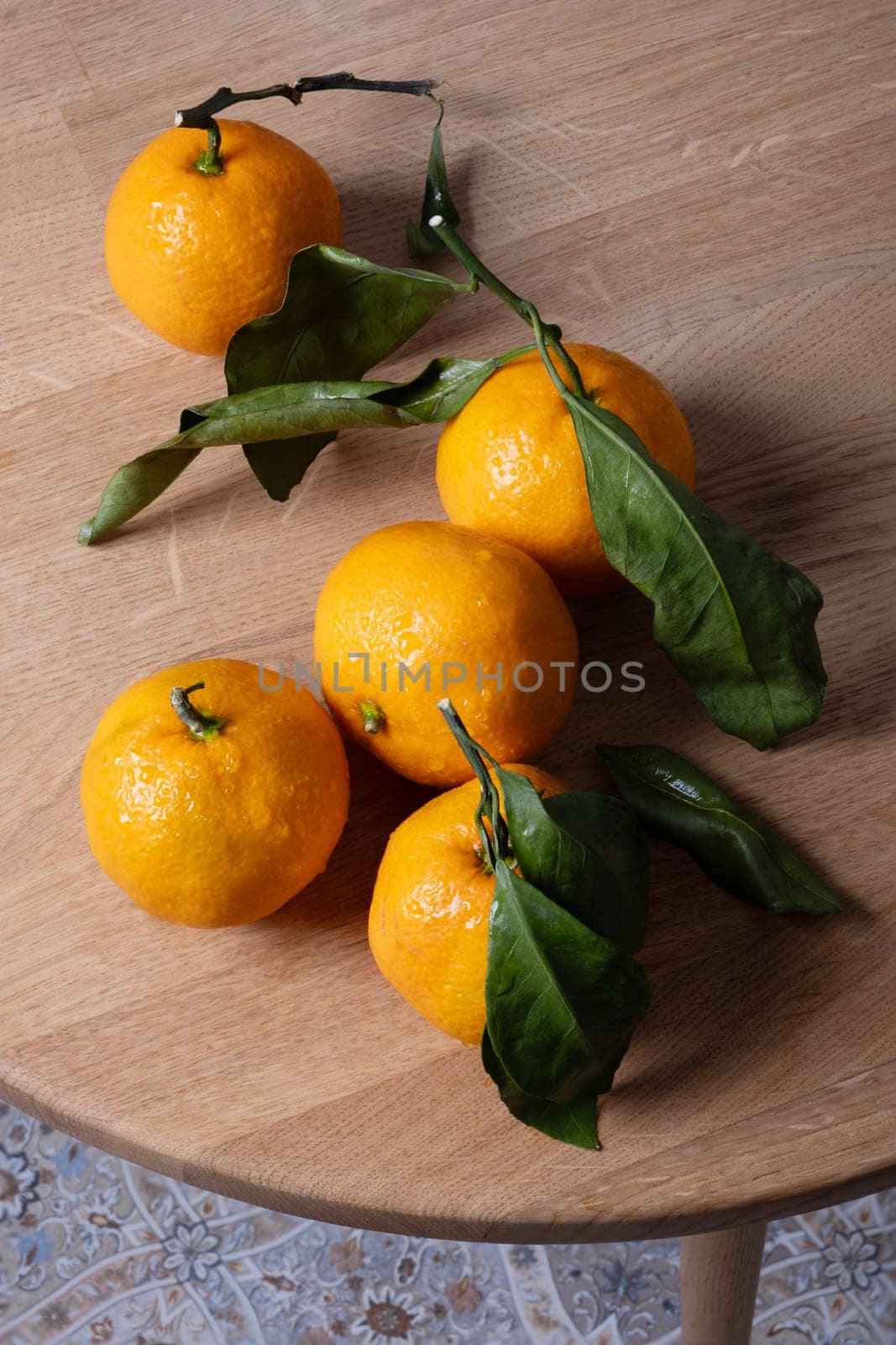 Several ripe tangerines with leaves lie on a table. Selective focus. by OlgaGubskaya