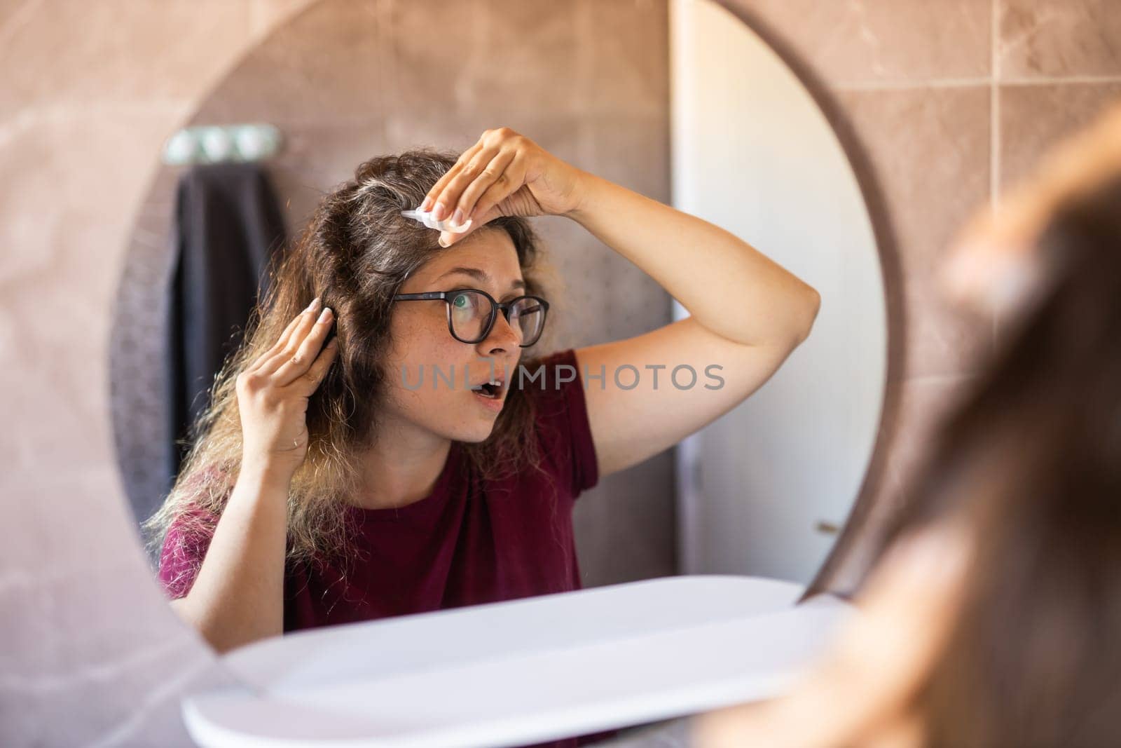 Gray haired surprised caucasian middle aged woman looking at grey hair head in mirror reflection