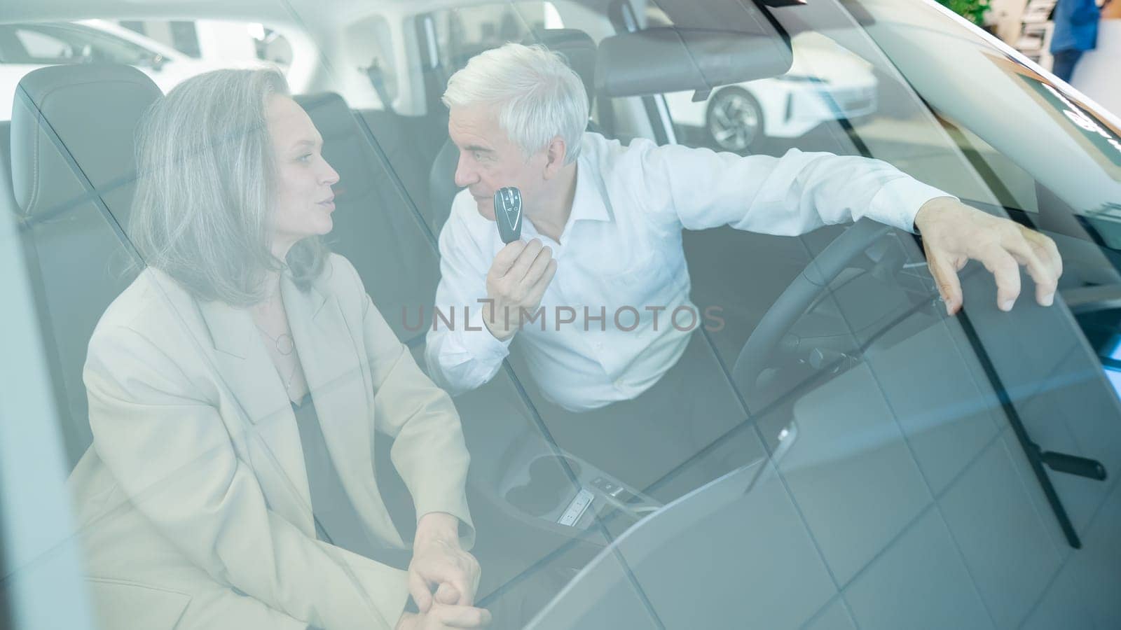 Mature Caucasian couple sitting in a new car and rejoicing at the purchase. View through the windshield. by mrwed54