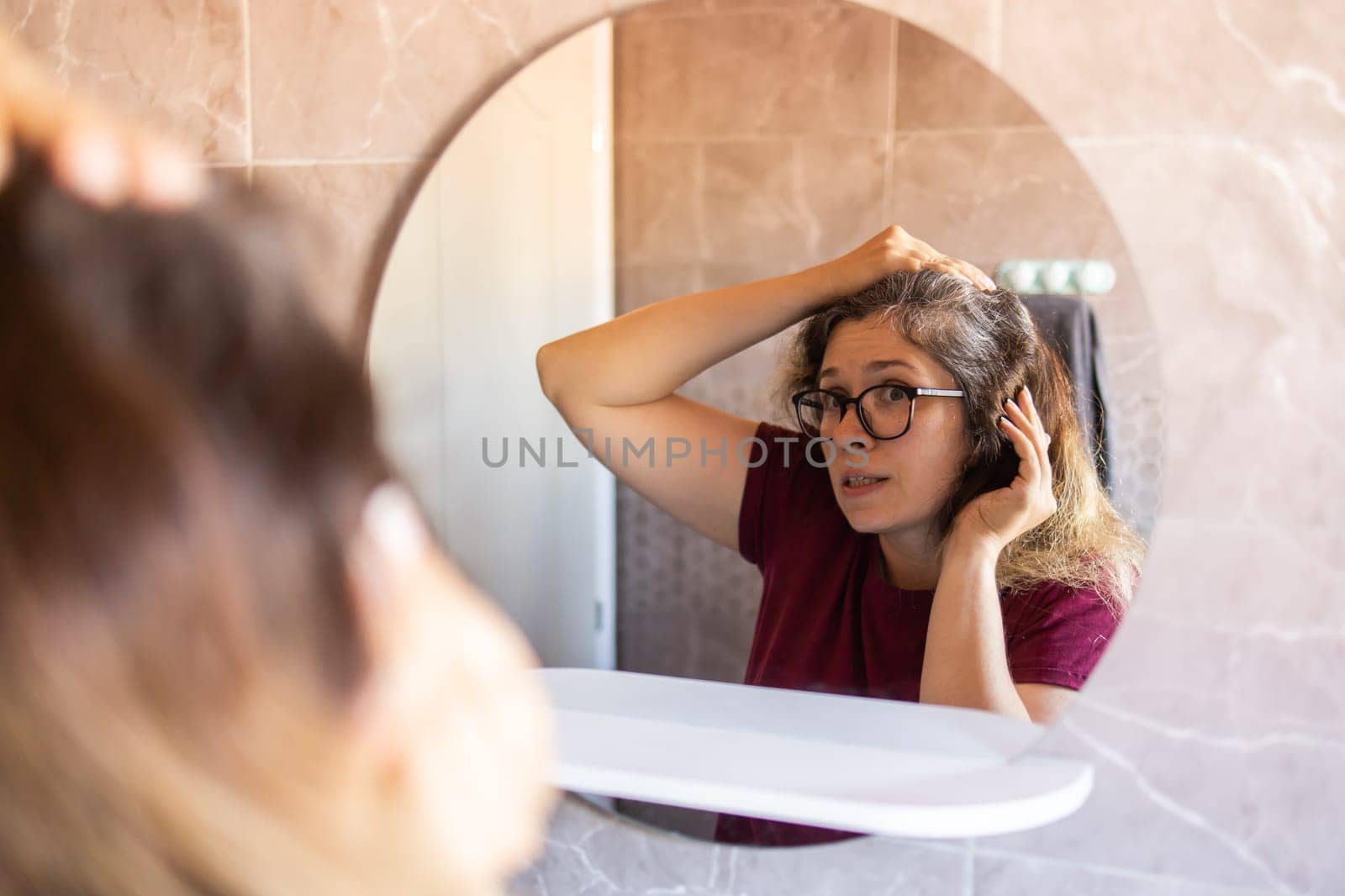 Gray haired surprised caucasian middle aged woman looking at grey hair head in mirror reflection