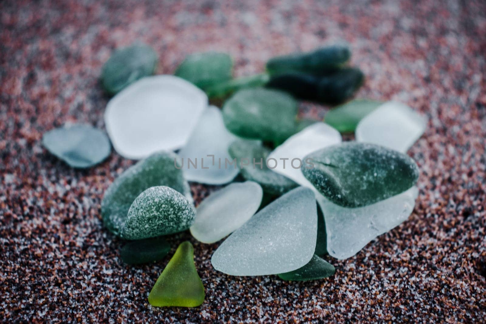 Sand beach and glass stones concept photo. Glass stones from broken bottles polished by the sea. Front view photography with blurred background. High quality picture for wallpaper, travel blog