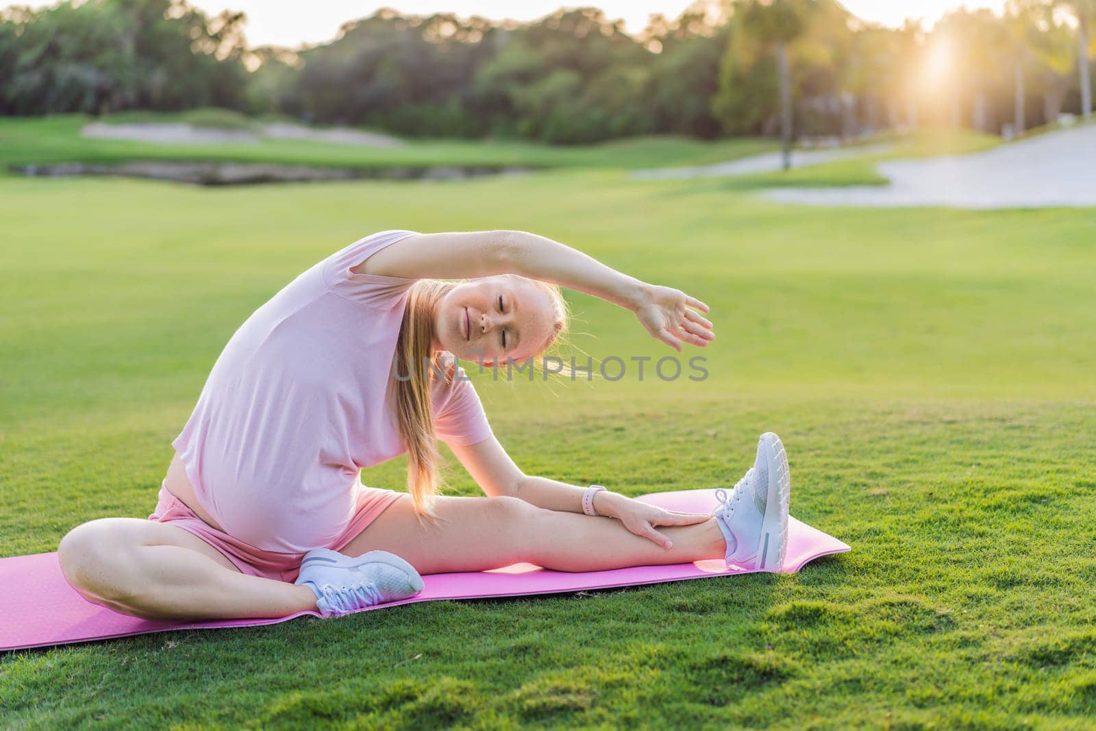 Energetic pregnant woman takes her workout outdoors, using an exercise mat for a refreshing and health-conscious outdoor exercise session by galitskaya