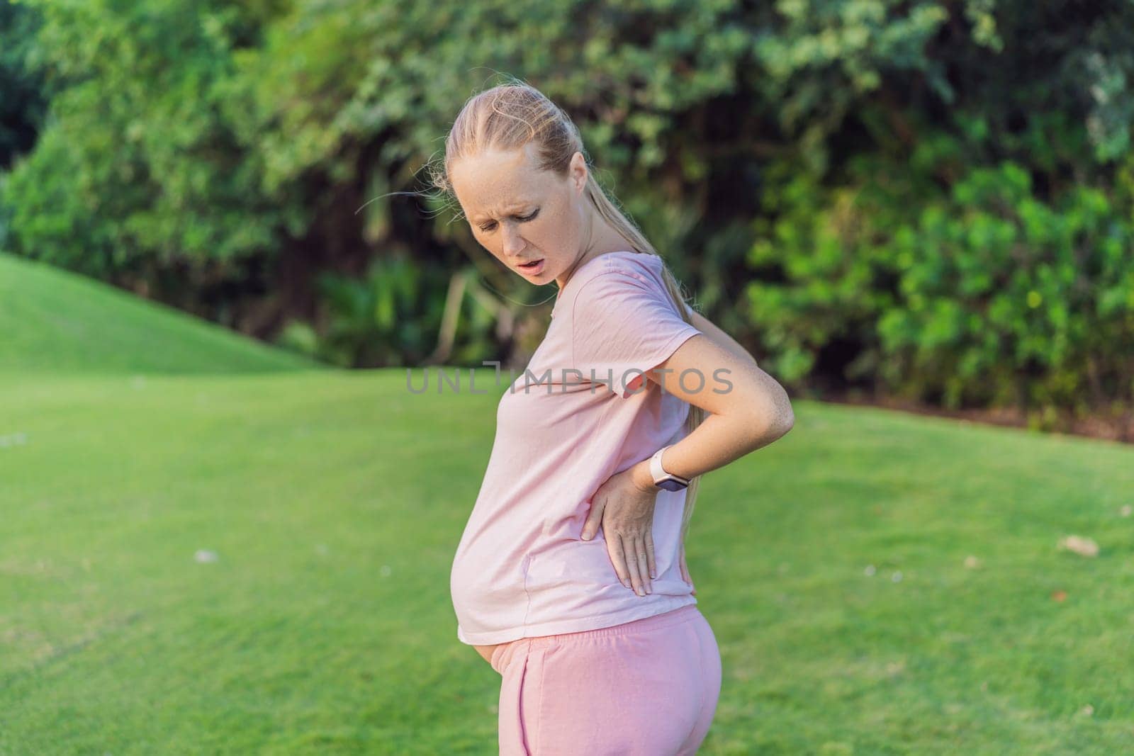 Expectant woman experiences back pain outdoors, seeking relief and comfort during pregnancy with a gentle outdoor stretch or rest by galitskaya