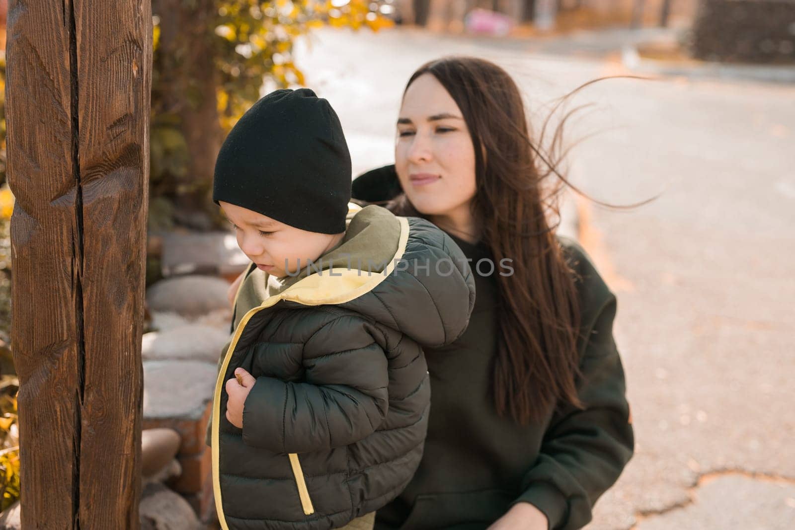Cute little asian boy stands with millennial mother outdoors. Happy child walking in autumn park. Toddler baby boy wears trendy jacket and hat. Autumn fashion. Stylish child outside. by Satura86