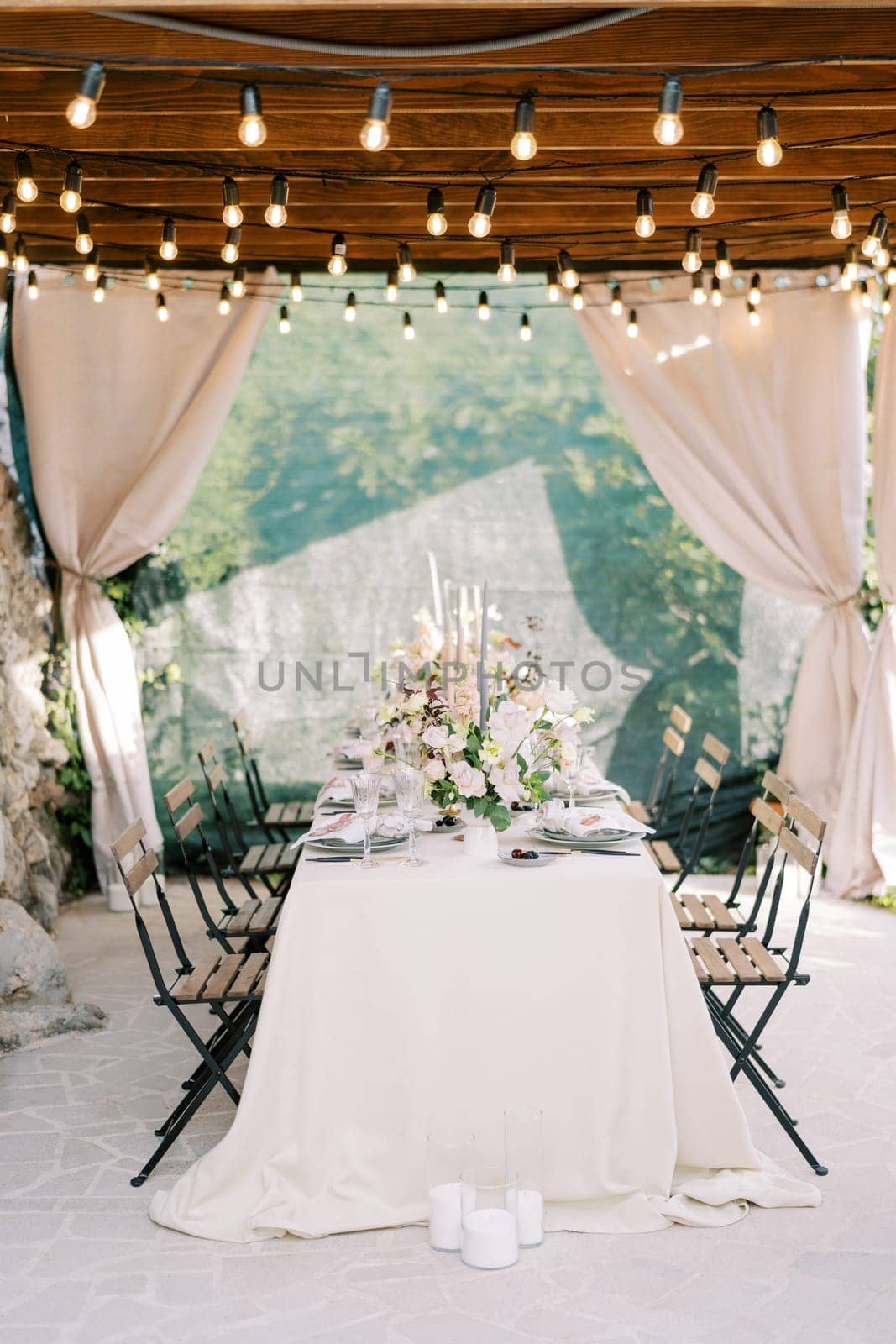 Laid table with bouquets of flowers stands on the terrace of an old house under a wooden canopy with curtains. High quality photo