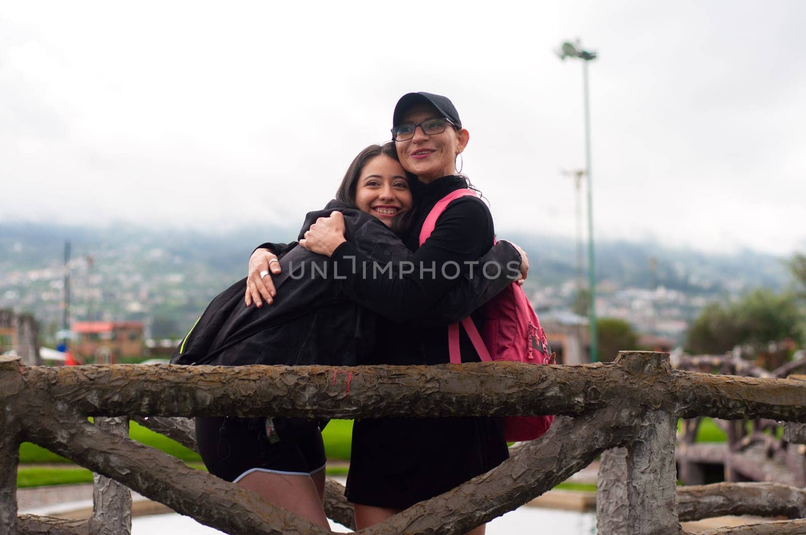 Mother and daughter in black sportswear hugging on a wooden bridge in a natural environment, both are very happy. High quality photo