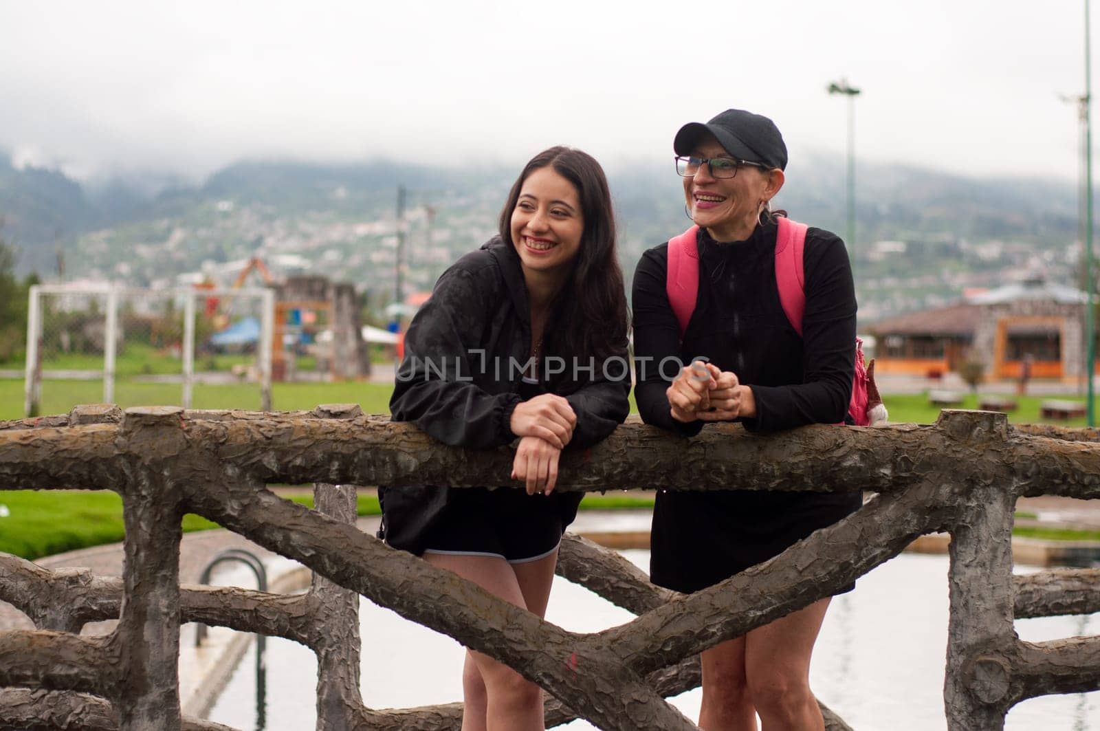 mother and daughter on a wooden bridge smiling together looking to their right. mother's love in a park. women's day. High quality photo