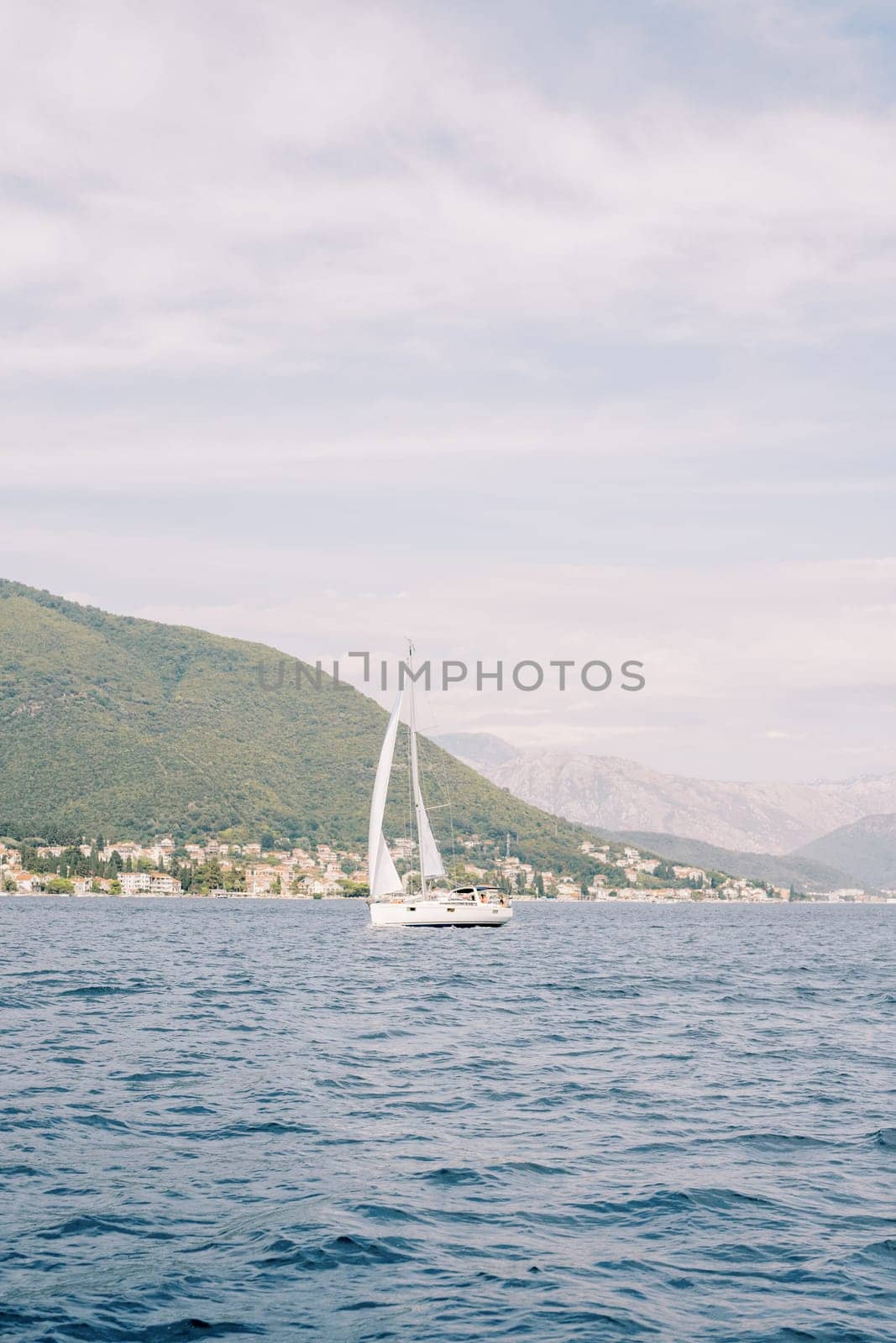 White sailing yacht sails along the mountainous coast by Nadtochiy