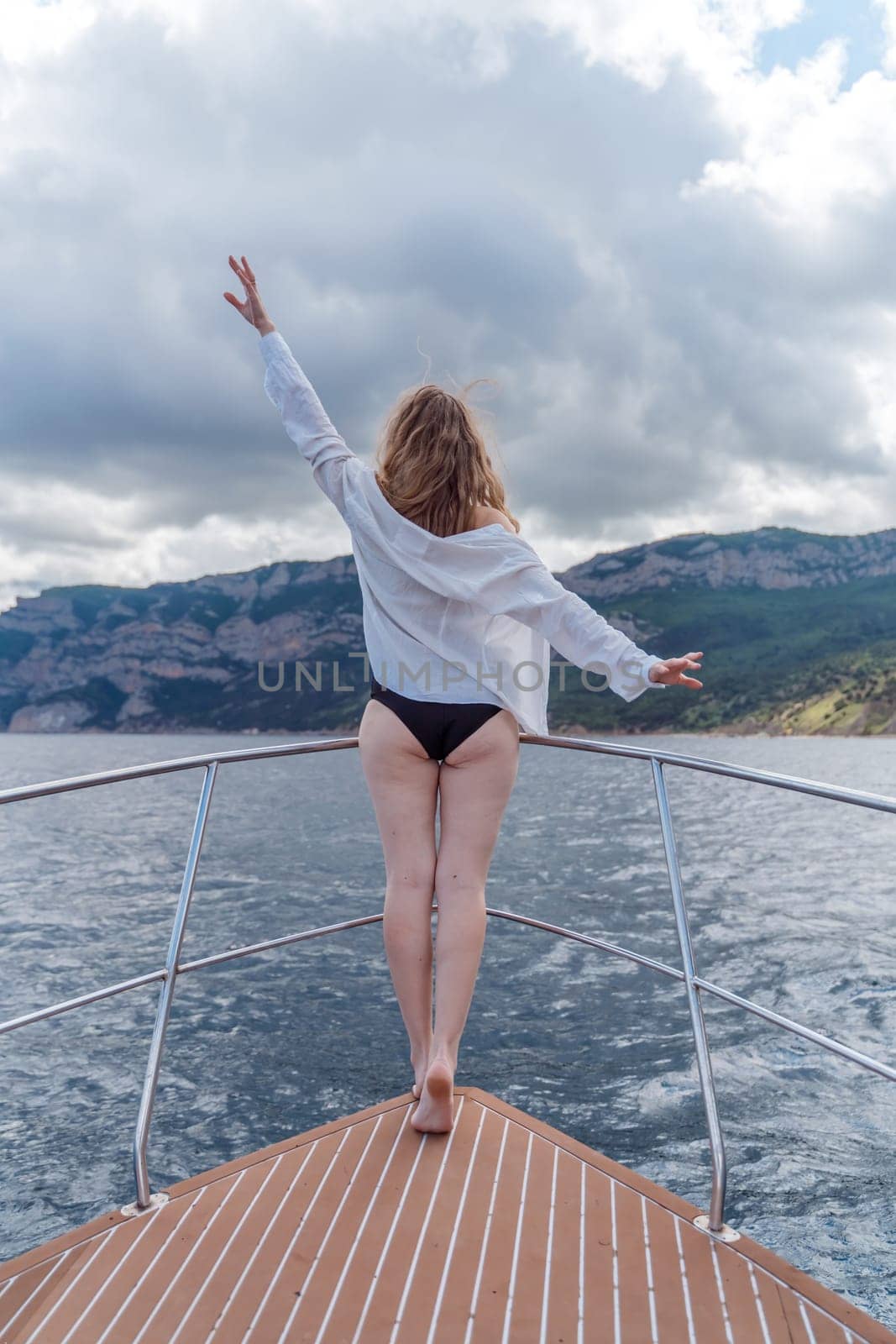 Woman on a yacht. Happy model in a swimsuit posing on a yacht against a blue sky with clouds and mountains.