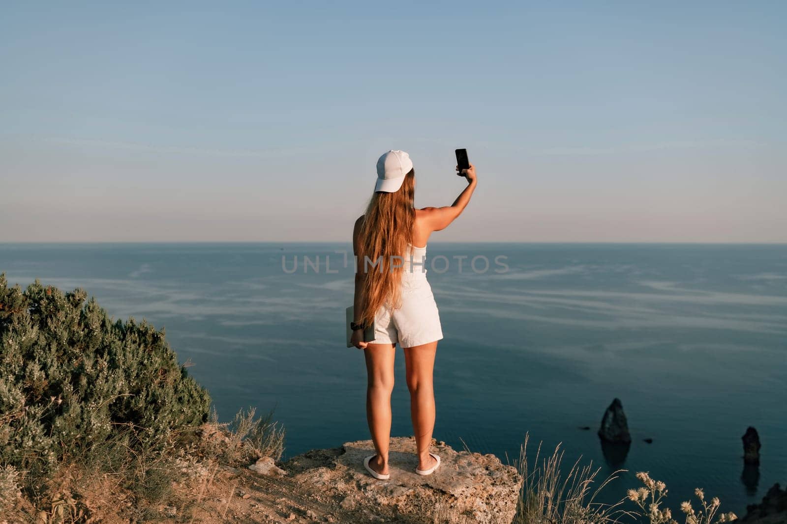 Selfie woman in a cap, white tank top and shorts makes a selfie shot mobile phone post photo social network outdoors on the background of the sea beach people vacation lifestyle travel concept