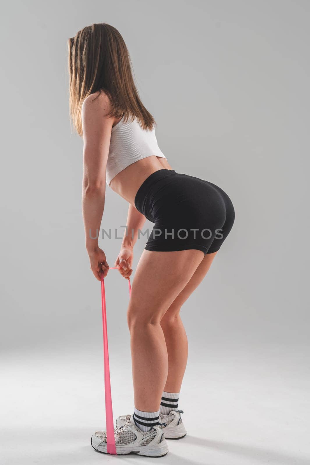 Caucasian woman doing exercises with fitness elastic band on white background. Vertical photo. by mrwed54