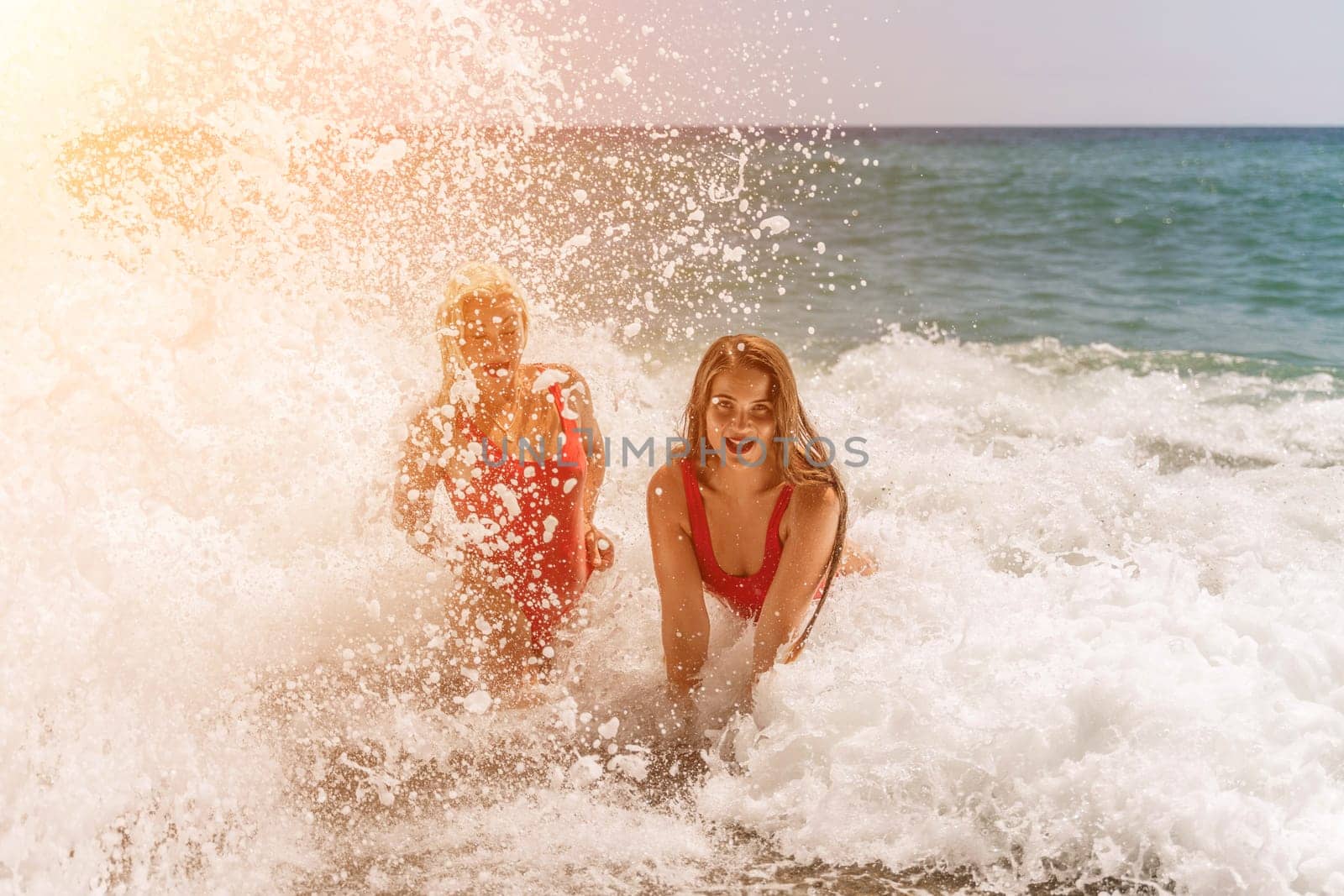 Women ocean play. Seaside, beach daytime, enjoying beach fun. Two women in red swimsuits enjoying themselves in the ocean waves. by Matiunina