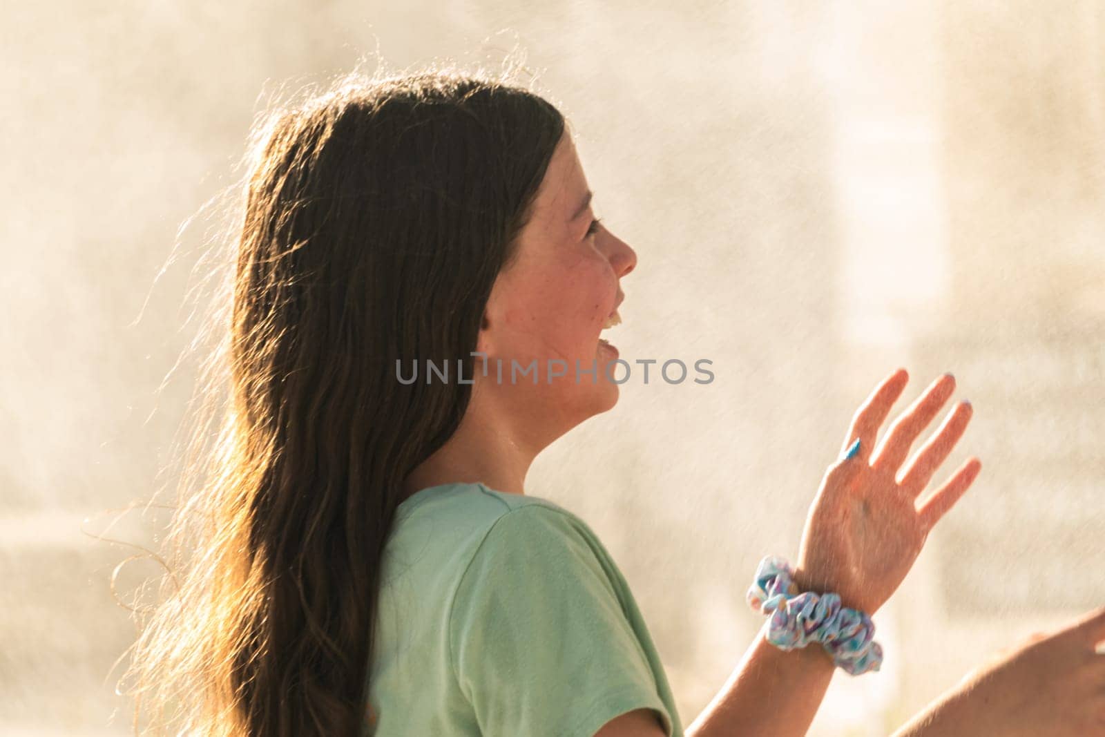 A joyful young girl gleefully gets soaked in refreshing water mist during a hot summer day.