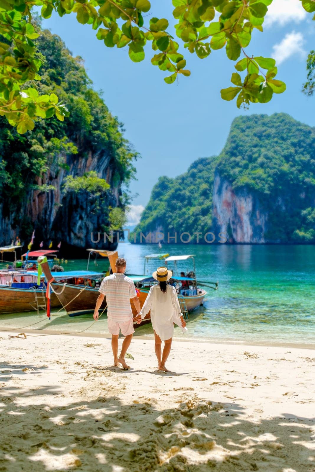 Koh Lao Lading Island near Koh Hong Krabi Thailand, is a beautiful beach with longtail boats, a couple of European men and an Asian woman on the beach. Couple on a boat trip in Krabi Thailand