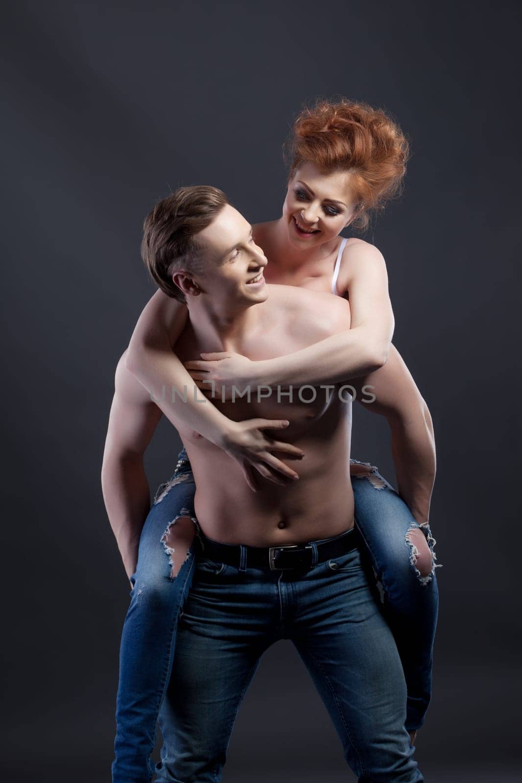 Happy young couple touts jeans. Studio photo, on gray background