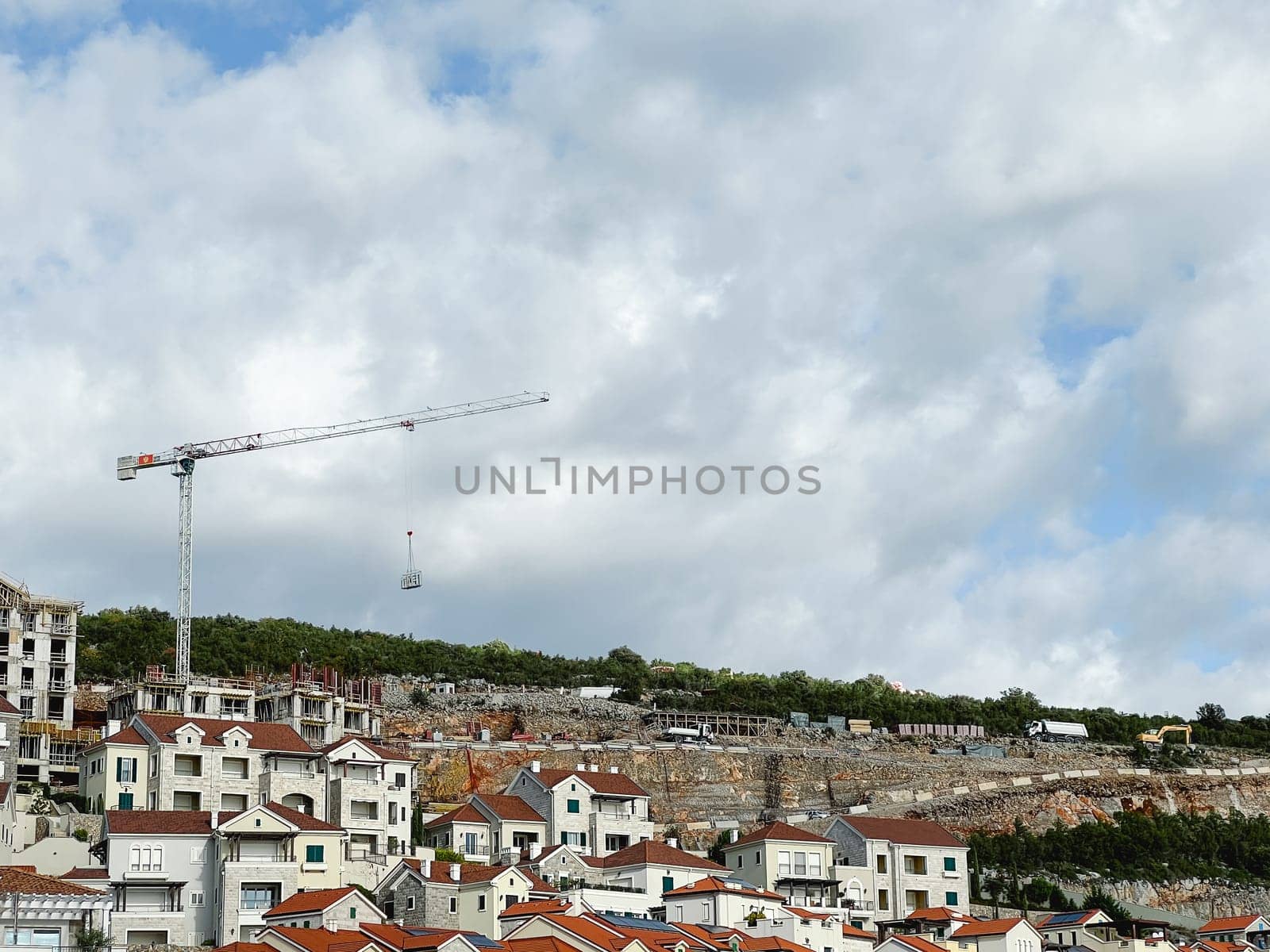 Construction crane builds a resort town with colorful buildings on a mountainside by Nadtochiy