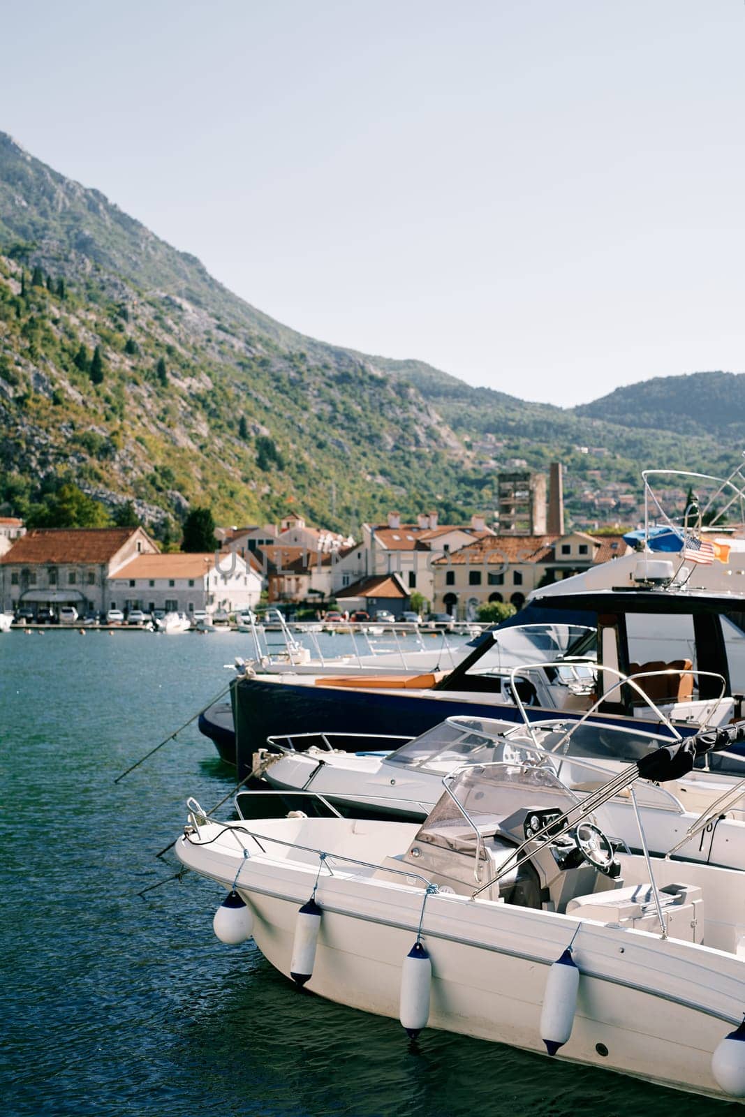 Motorboats are moored along the shore overlooking ancient houses at the foot of the mountains. Kotor, Montenegro. High quality photo