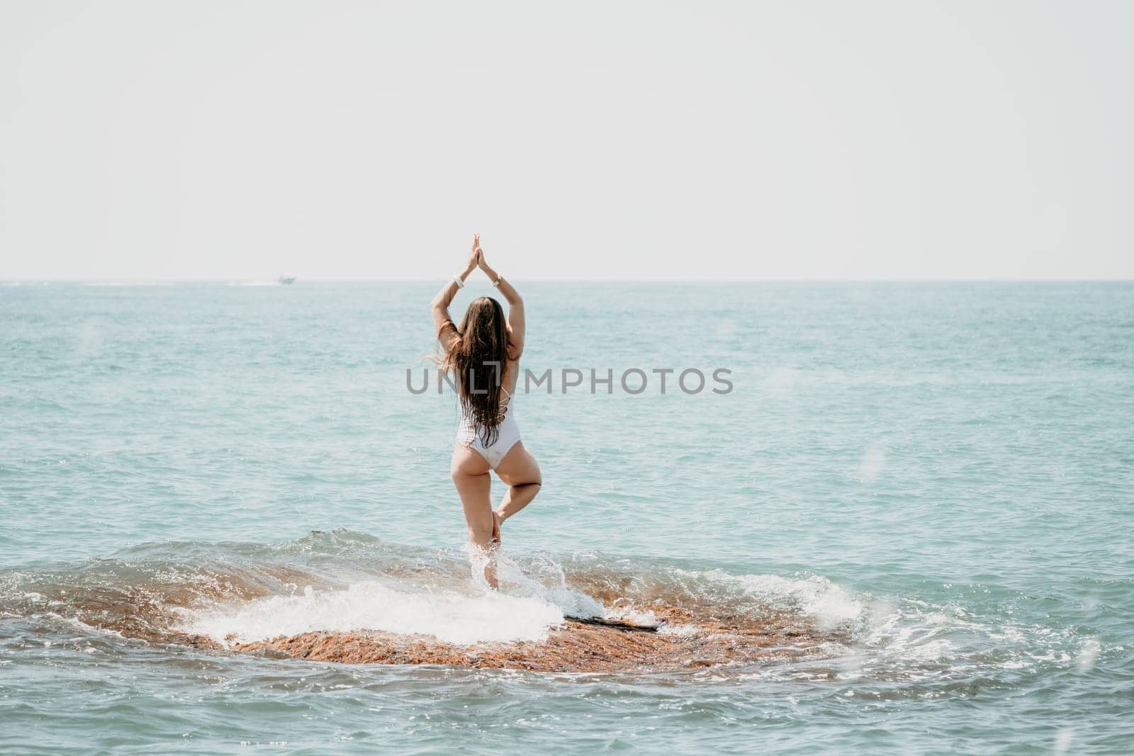 Woman sea yoga. Back view of free calm happy satisfied woman with long hair standing on top rock with yoga position against of sky by the sea. Healthy lifestyle outdoors in nature, fitness concept by panophotograph