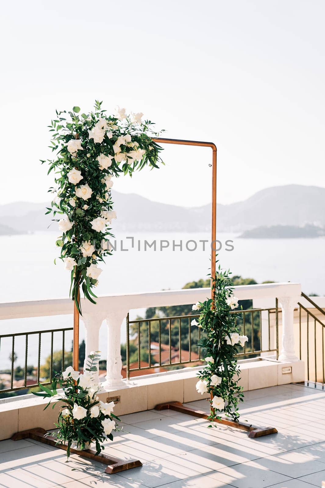 Rectangular wedding arch stands on a terrace above the sea against the backdrop of mountains. High quality photo