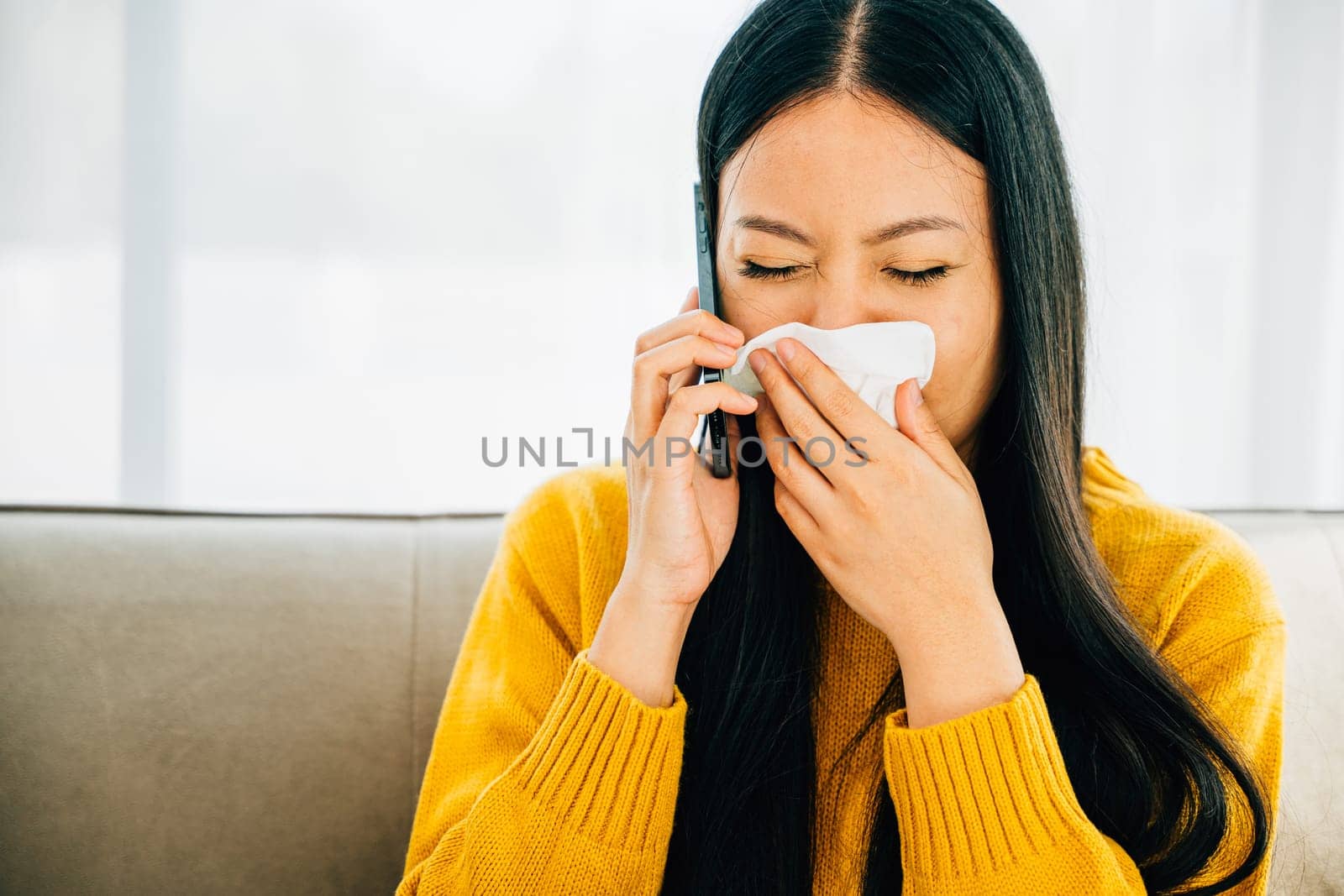 Sitting on sofa sick woman calls doctor blowing wiping nose sneezing into tissue. ill young girl consults practitioner via phone about flu symptoms seeking medicine. Illustrating patient care at home.