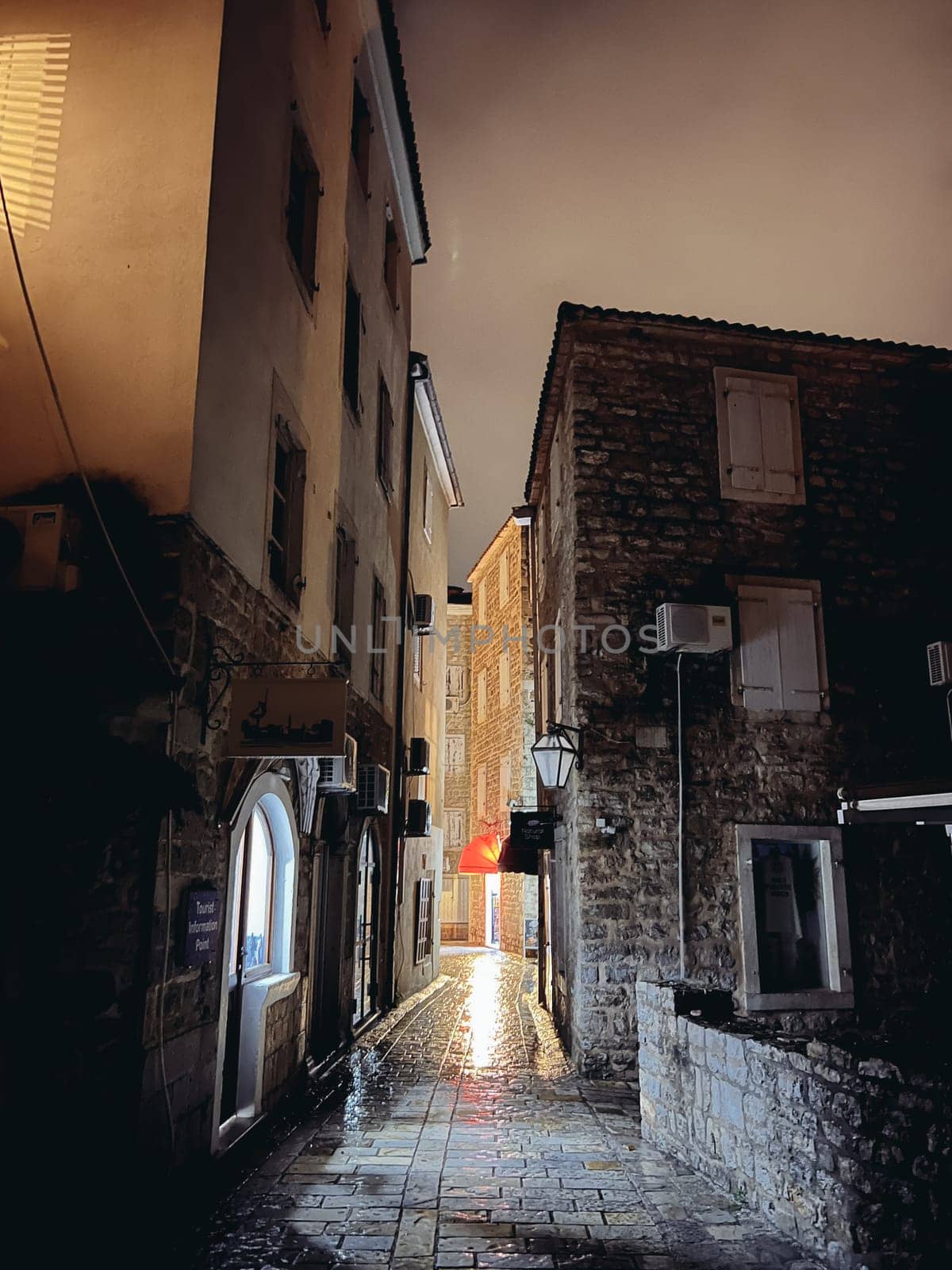 Budva, Montenegro - 25 december 2022: Narrow illuminated ancient street with luminous windows by Nadtochiy