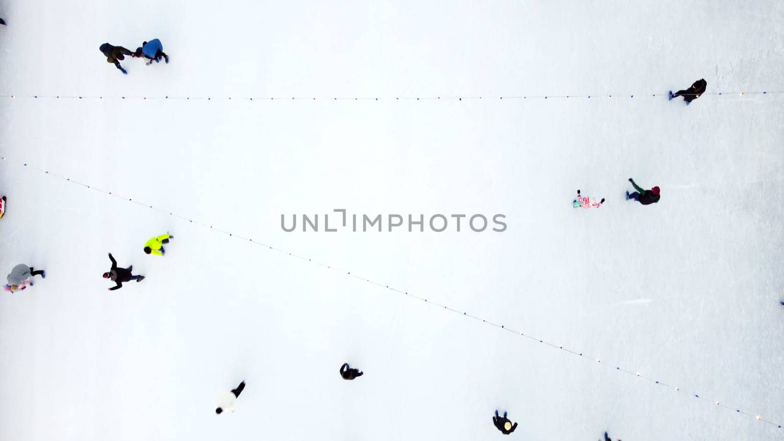 Many people skating on white ice skating rink outdoors on winter day top view. Aerial drone view. New Year Christmas celebration holidays recreation sport enjoying lifestyle sportive fun background.