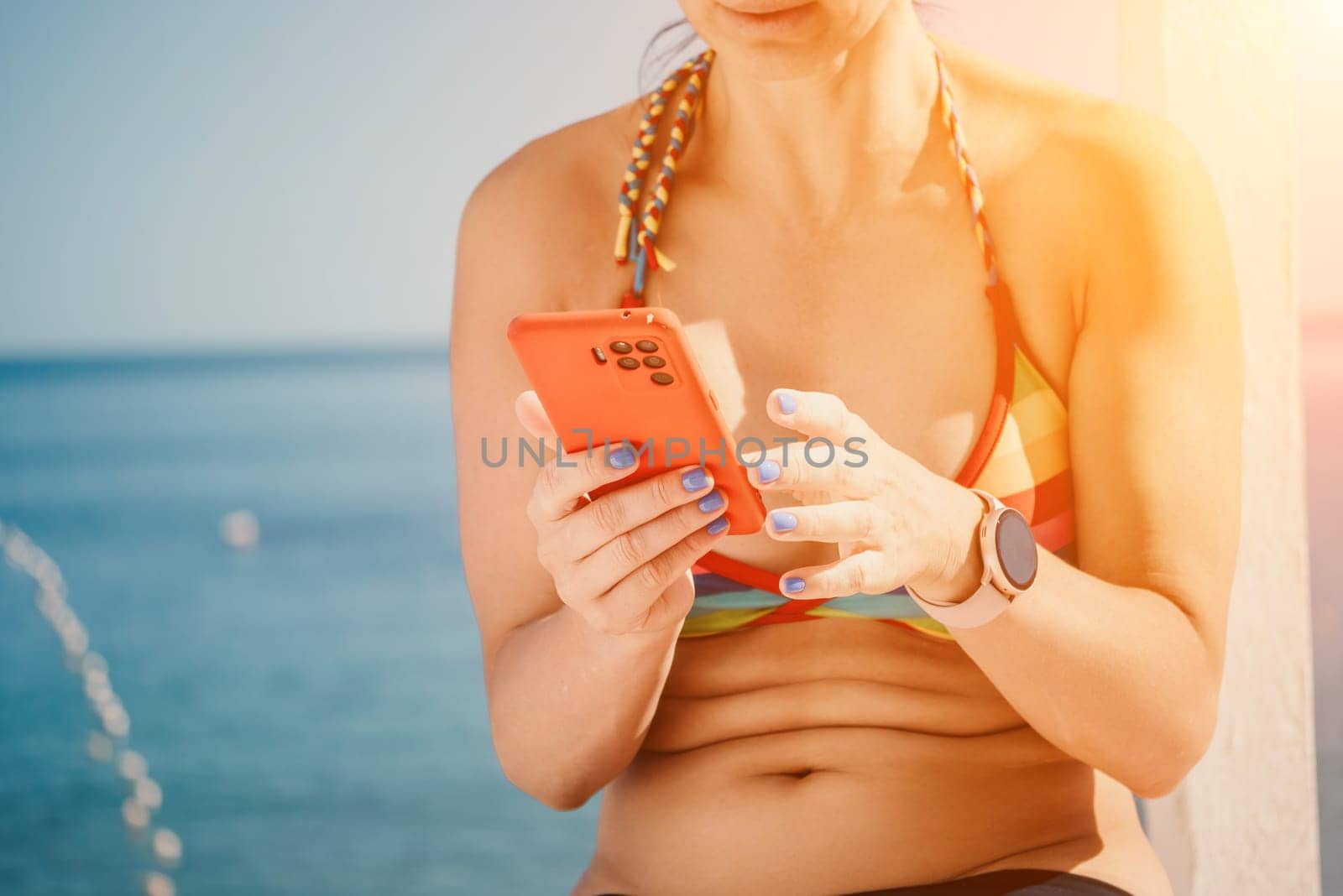 Woman in rainbow bikini. Happy tanned girl in rainbow swimsuit at seaside, blue sea water in background