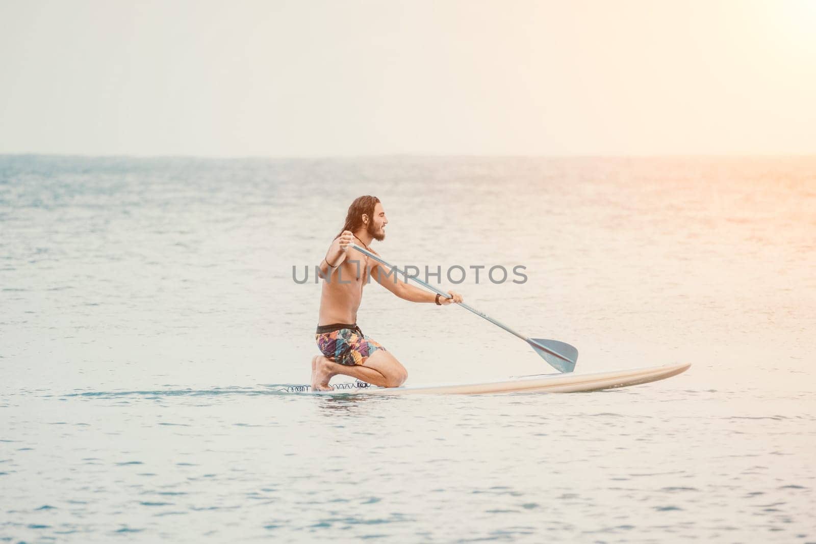 Sea woman and man on sup. Silhouette of happy young woman and man, surfing on SUP board, confident paddling through water surface. Idyllic sunset. Active lifestyle at sea or river. by panophotograph