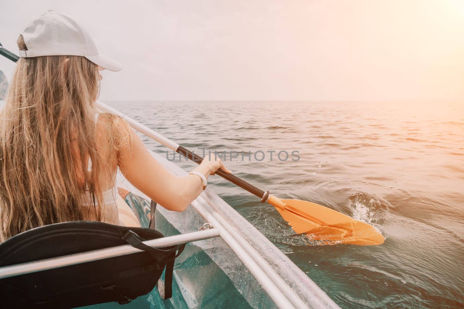 Woman in kayak back view. Happy young woman with long hair floating in transparent kayak on the crystal clear sea. Summer holiday vacation and cheerful female people relaxing having fun on the boat by panophotograph