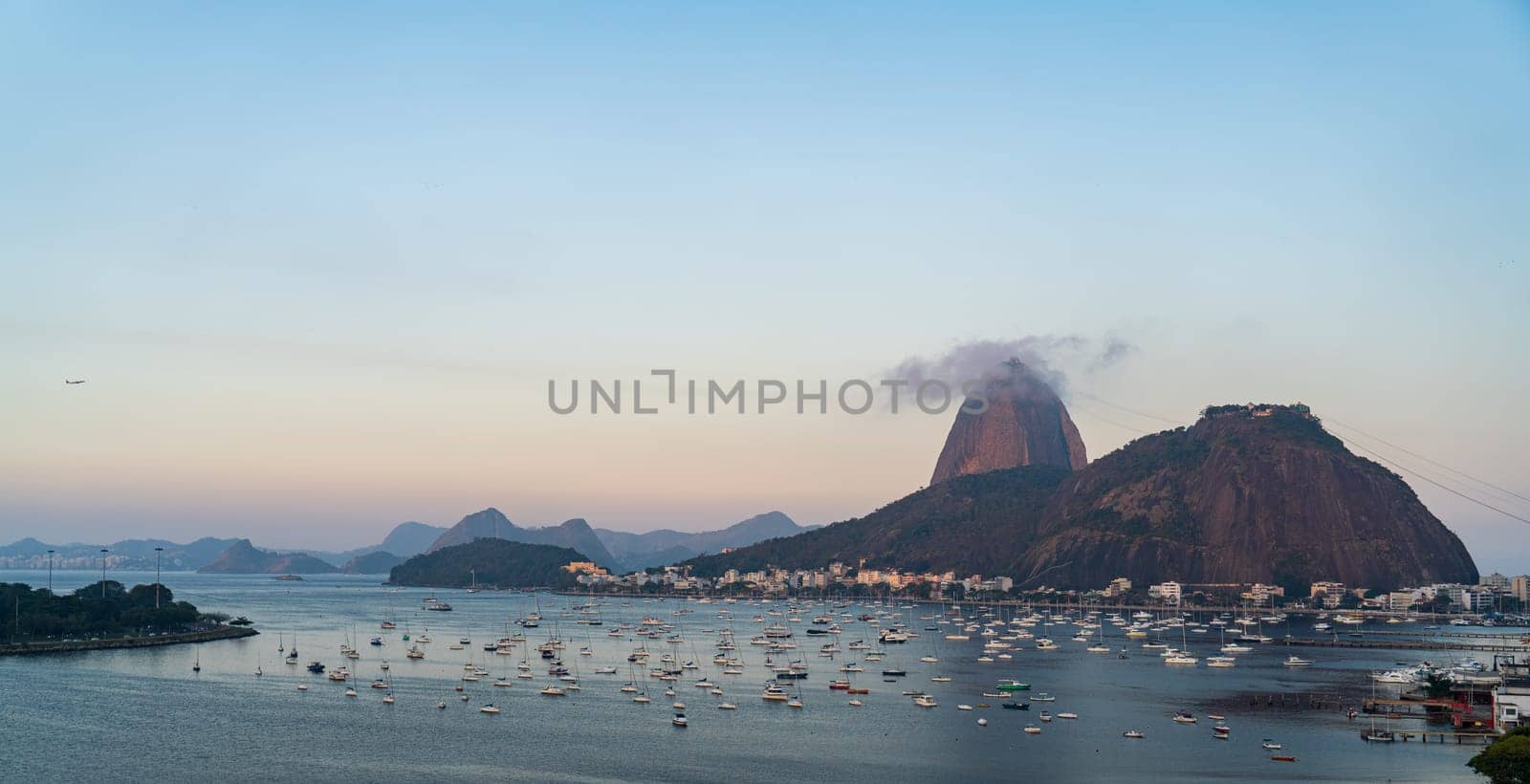 Serene evening with anchored boats in a bay, mountains in the distance, and city skyline of Rio de Janeiro