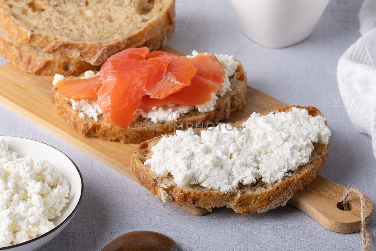 Sandwich with salted salmon and cottage cheese on a wooden table.