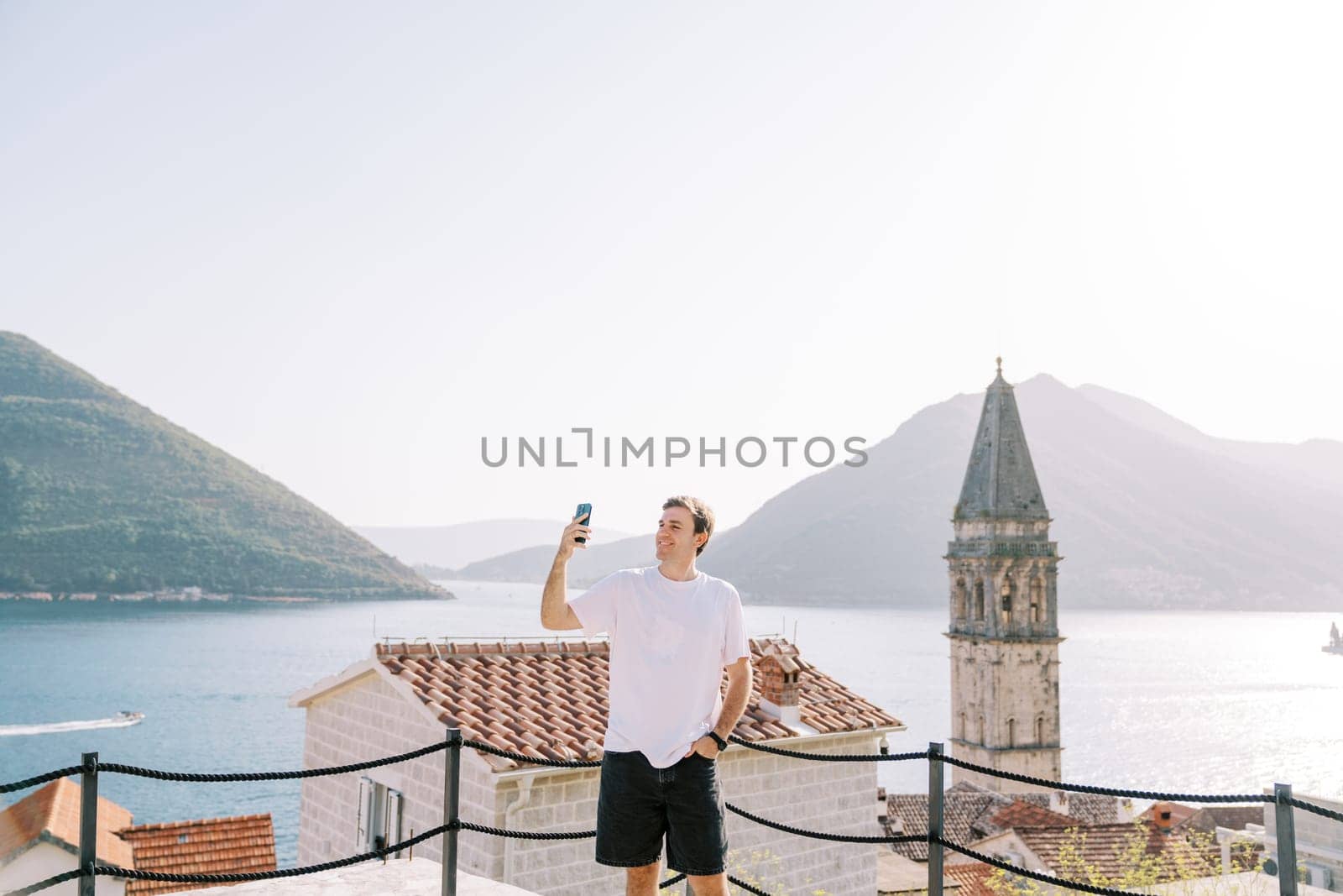 Smiling man takes a selfie on the platform overlooking the bell tower. Perast, Montenegro. High quality photo