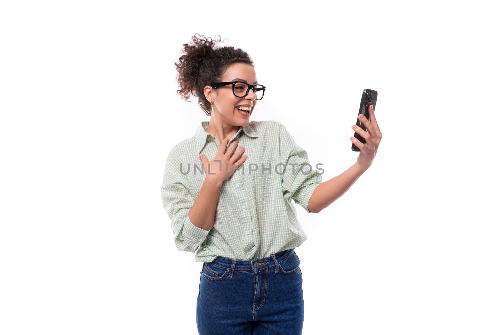 young surprised curly brunette blogger woman with glasses leads video broadcast using smartphone and online network.