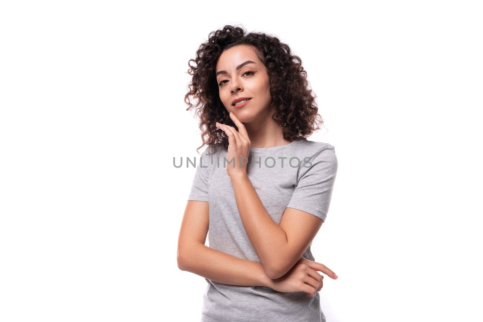 portrait of a pretty young european slim brunette woman with curly hair dressed in a gray t-shirt on a white background by TRMK