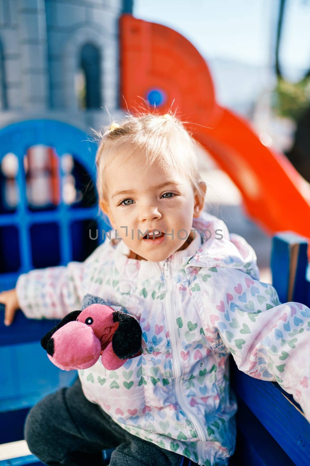 Little smiling girl sitting on a bench in the playground. High quality photo