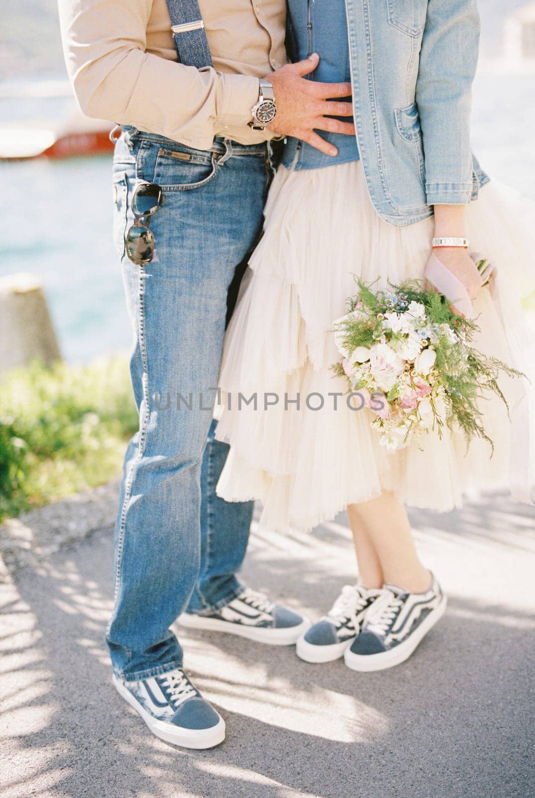 Groom hugs the waist of bride with a bouquet on the seashore. Cropped. Faceless. High quality photo