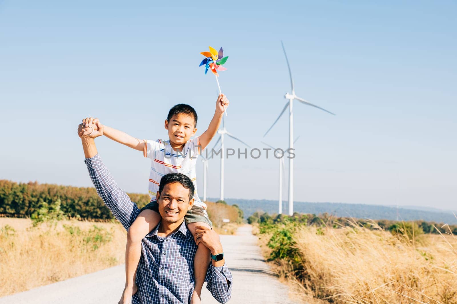 Father holds daughter with pinwheel enjoying. Family bonding near windmills signifies global innovation in renewable energy. A joyful moment in the community's pursuit of happiness. Father Day