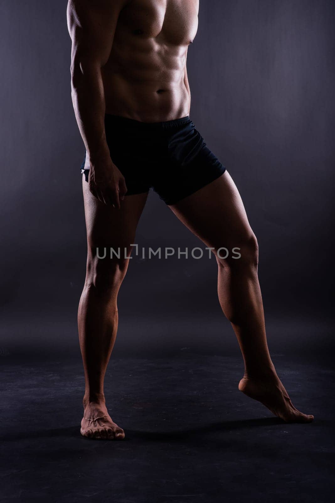 Muscular male legs, man in a studio, dark background