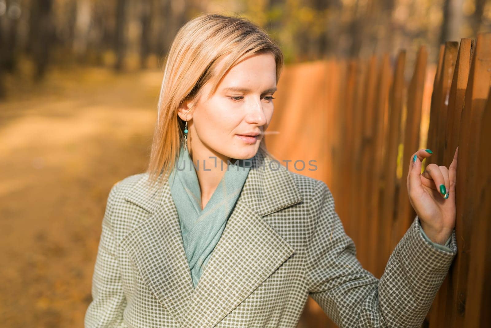 Blonde woman in elegant gray coat walks in the sunny autumn season park. Generation z and gen z youth concept