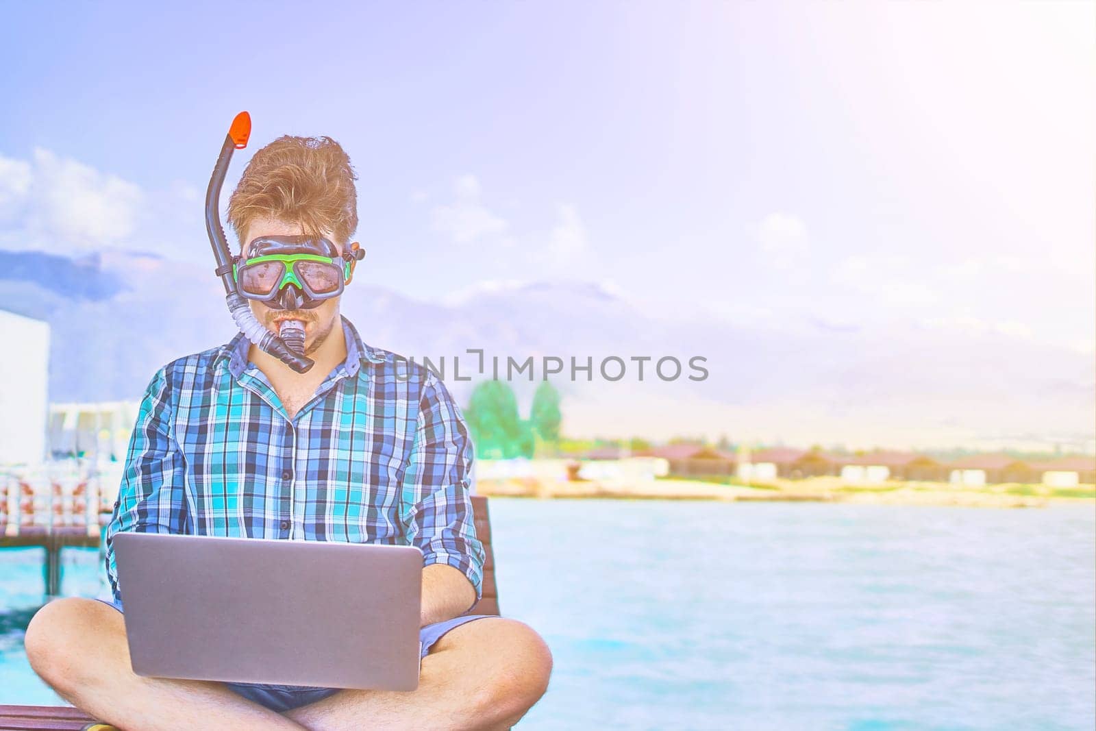 A man in an underwater mask, on vacation at sea, working at a computer.