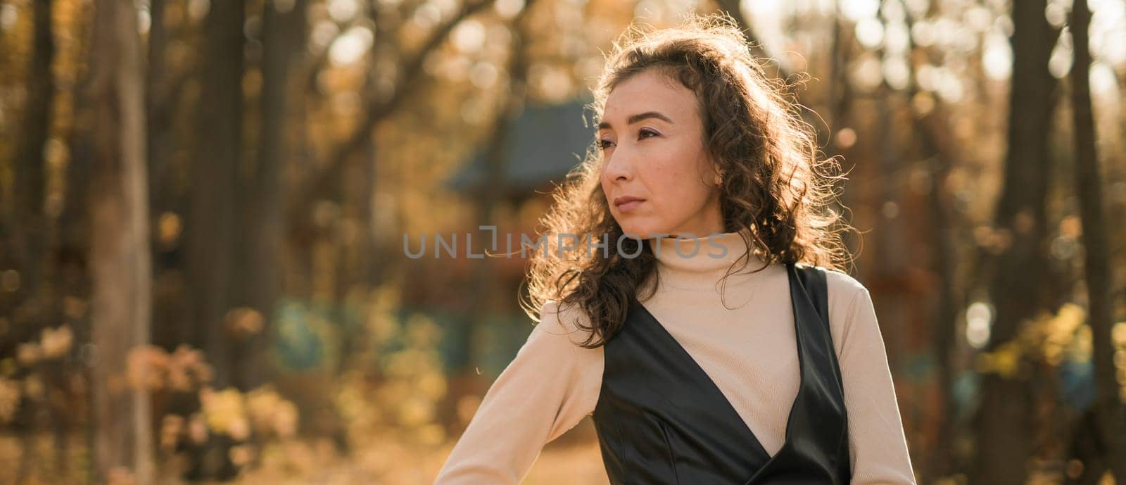 Attractive young woman walking in autumn park, happy mood and fashion style trend and curly long brown hair. Fall season and pretty female portrait. Millennial generation