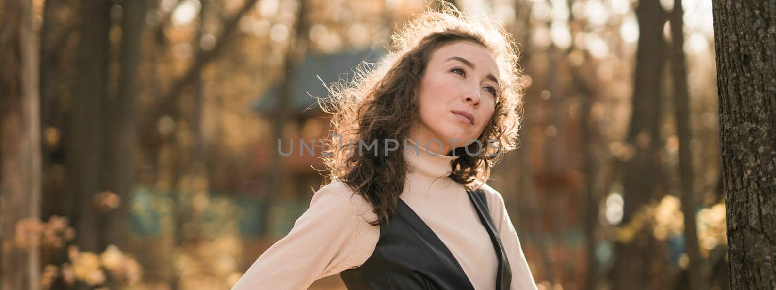 Attractive young woman walking in autumn park, happy mood and fashion style trend and curly long brown hair. Fall season and pretty female portrait. Millennial generation