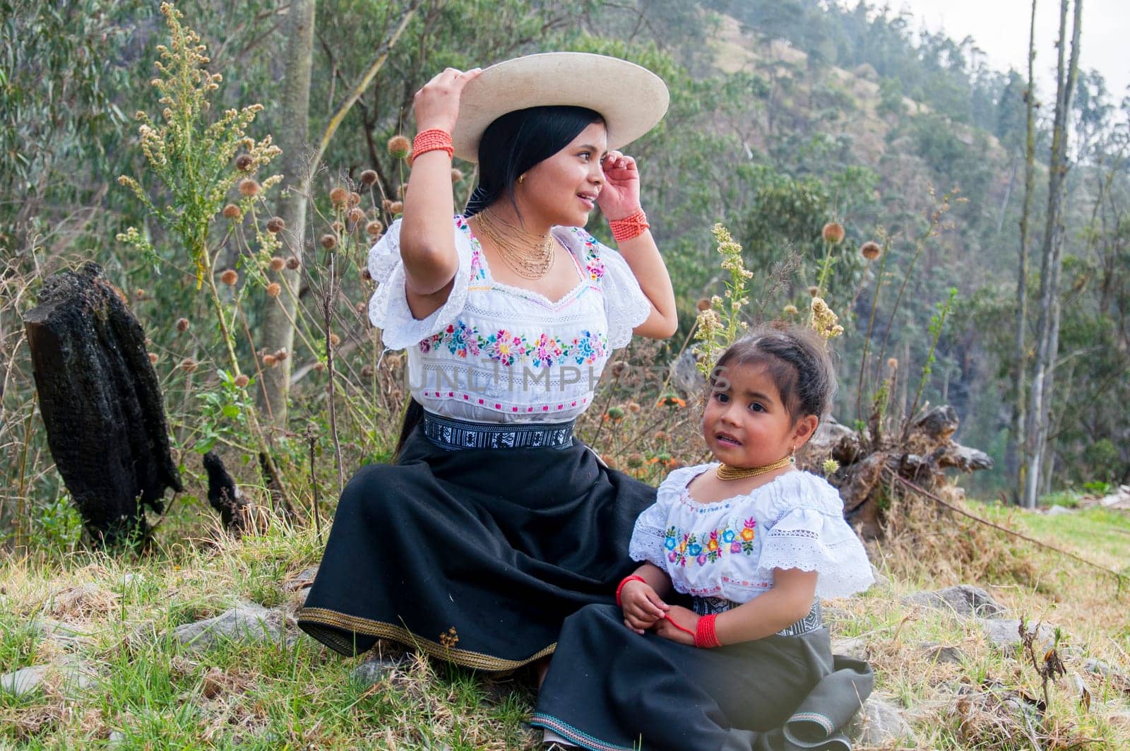 young mother and daughter enjoying a sunny day together in the ecuadorian amazon with their traditional attire and dresses from otavalo, ecuador. women's day. by Raulmartin