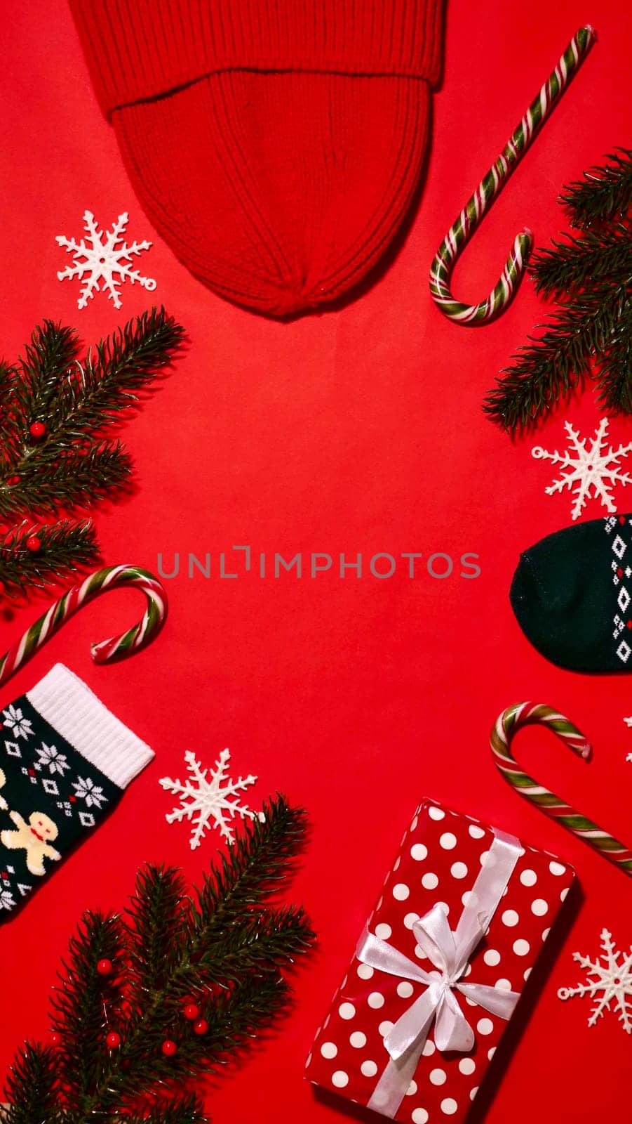 Festive Christmas Frame on Red Background on New Year 2024 with Branch, Gift, Hat, Candy Caramel, Snowflakes, Socks. Top view, close-up, flatlay, copy space, composition, vertical