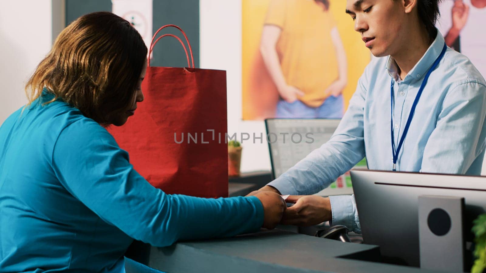 Store worker giving bag to shopaholic customer after paying for fashionable merchandise in modern boutique. African american woman purchasing stylish clothes and trendy accessories