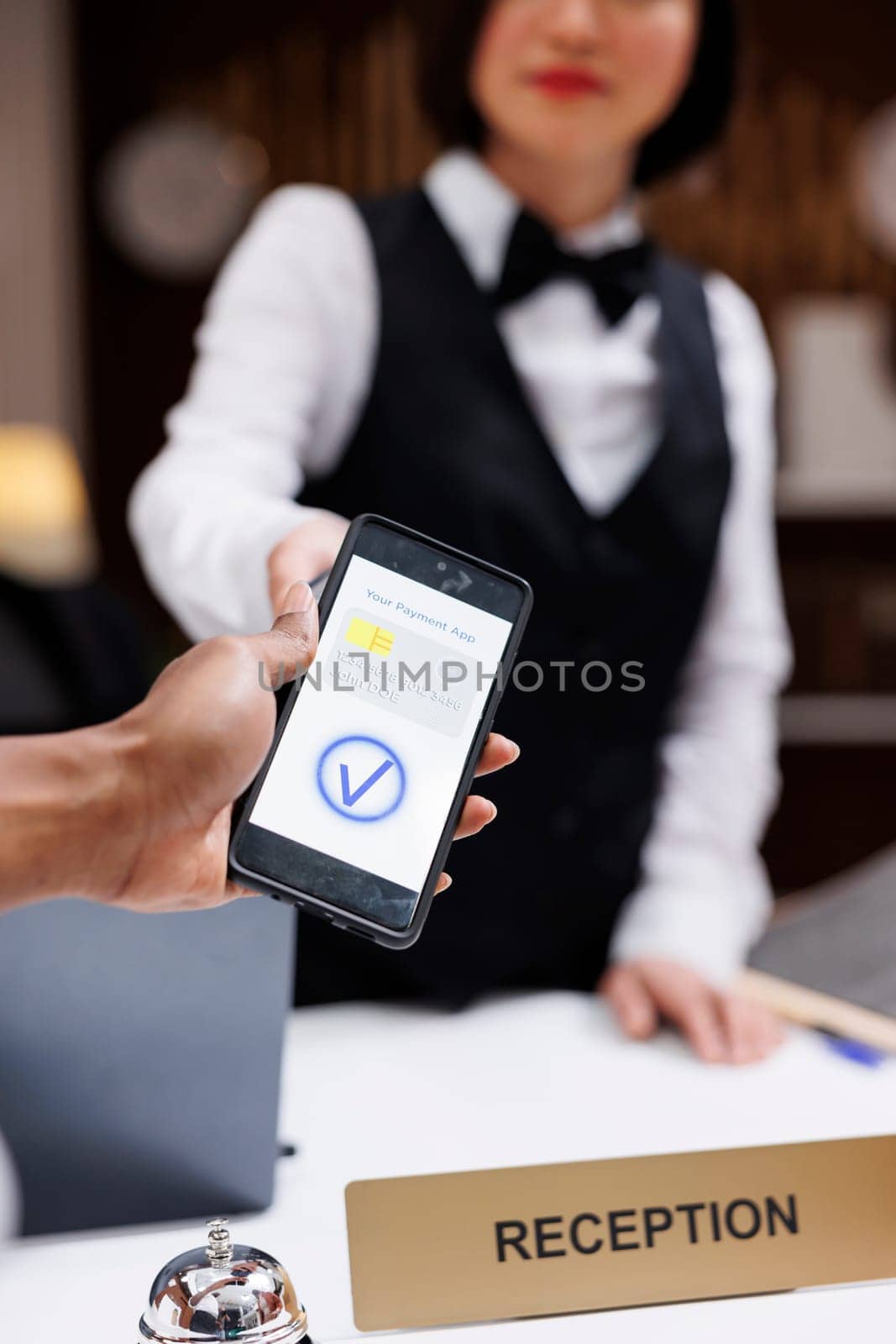 Guest paying with nfc on phone at pos terminal, hotel staff helping tourists with registration forms. Receptionist welcoming people, young man making payment for booking. Close up.