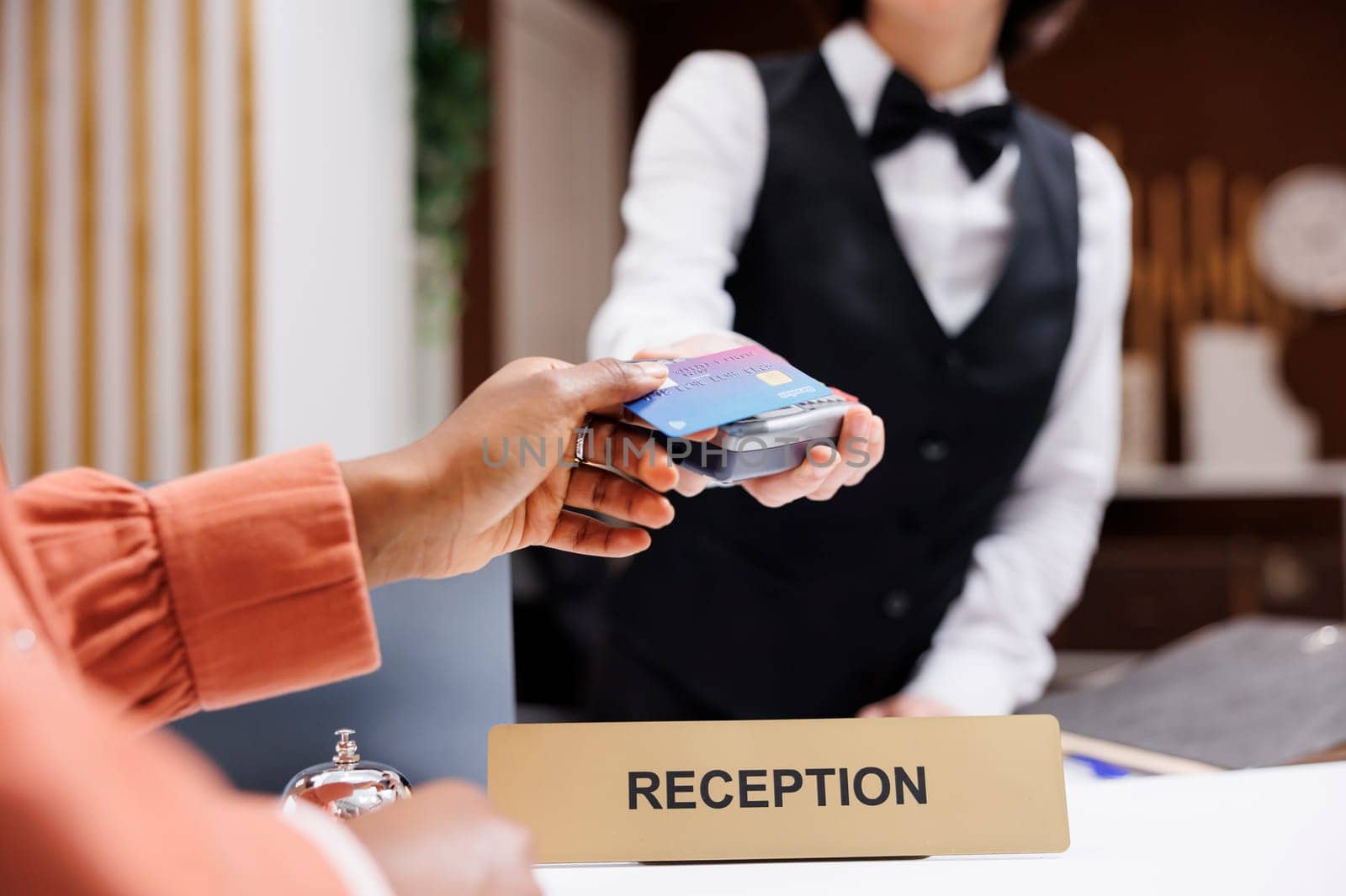 Female tourist paying at pos terminal in hotel lobby, using electronic payment at check in registration. Young resort guest using credit card at reception counter front desk. Close up.